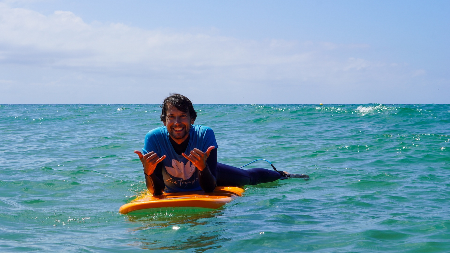 Surfeur débutant à l'eau allongé sur une planche Zeus orange