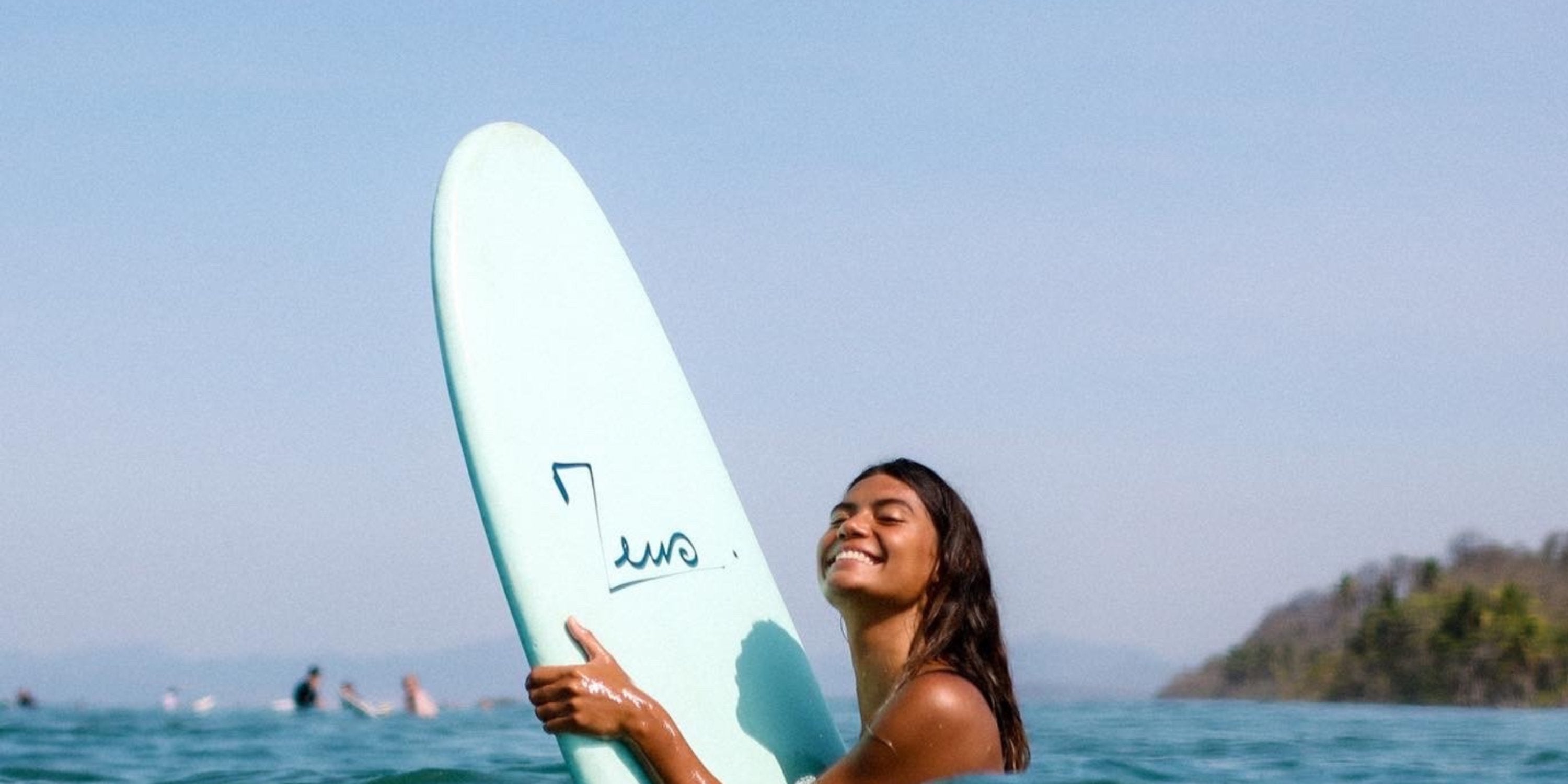 Une surfeuse souriante en d'attendre au pic une vague avec une planche de surf longboard avec un logo zeus