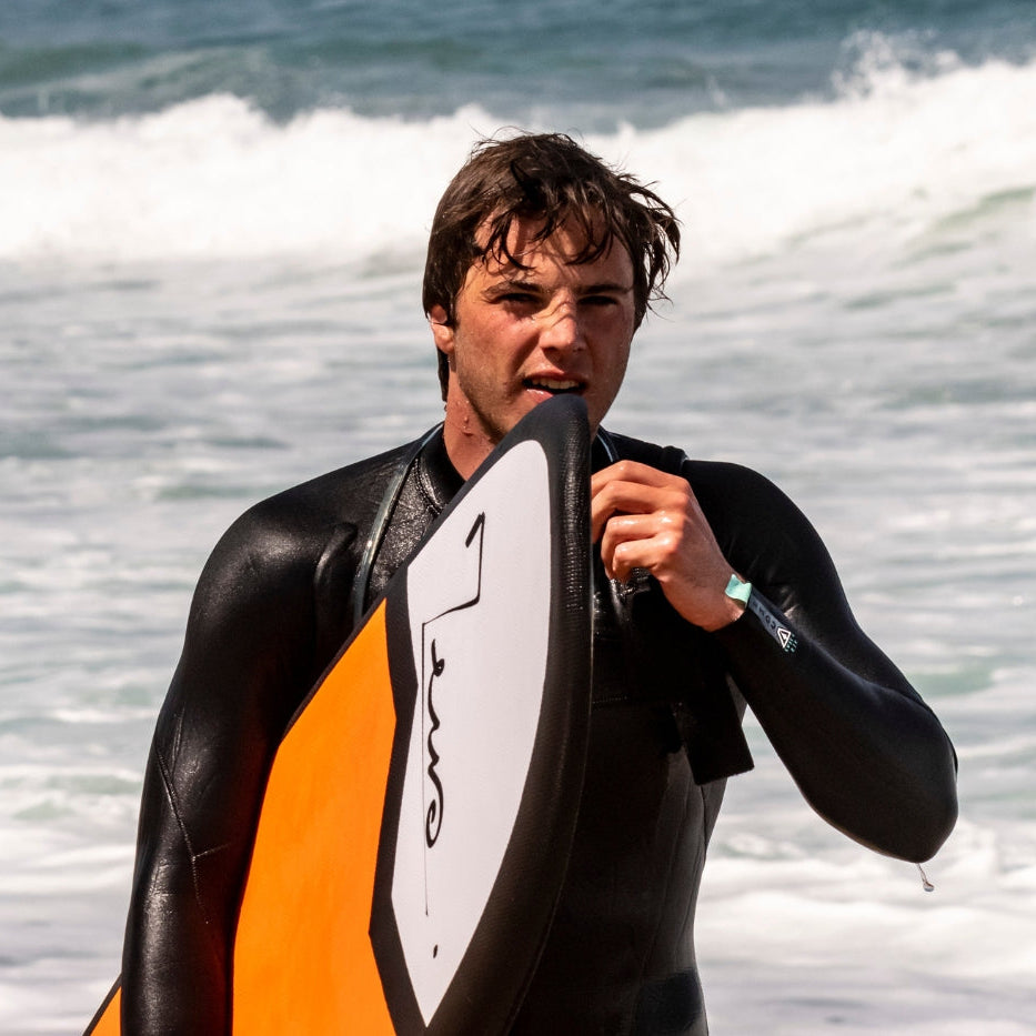 Planche de surf en mousse Zeus orange sur la plage avec un surfeur