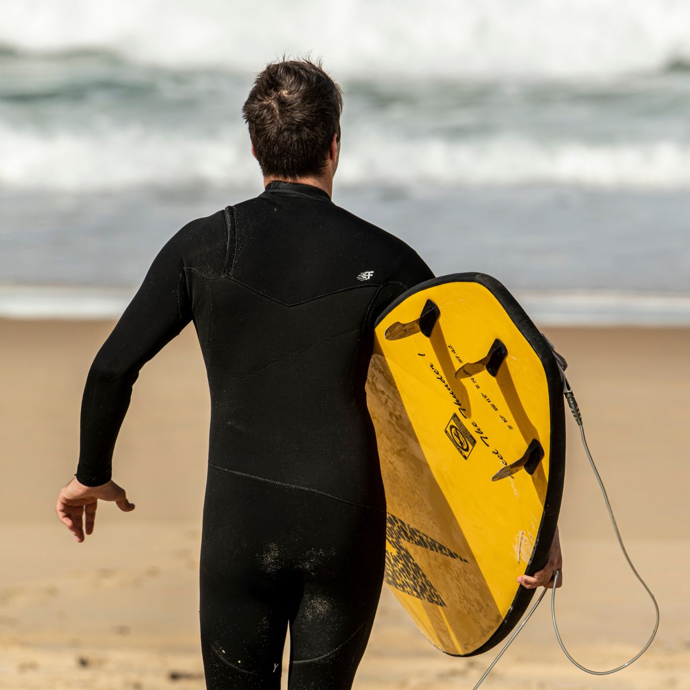 Surfeur en train de porter une planche de surf jaune sur la plage de la marque Zeus