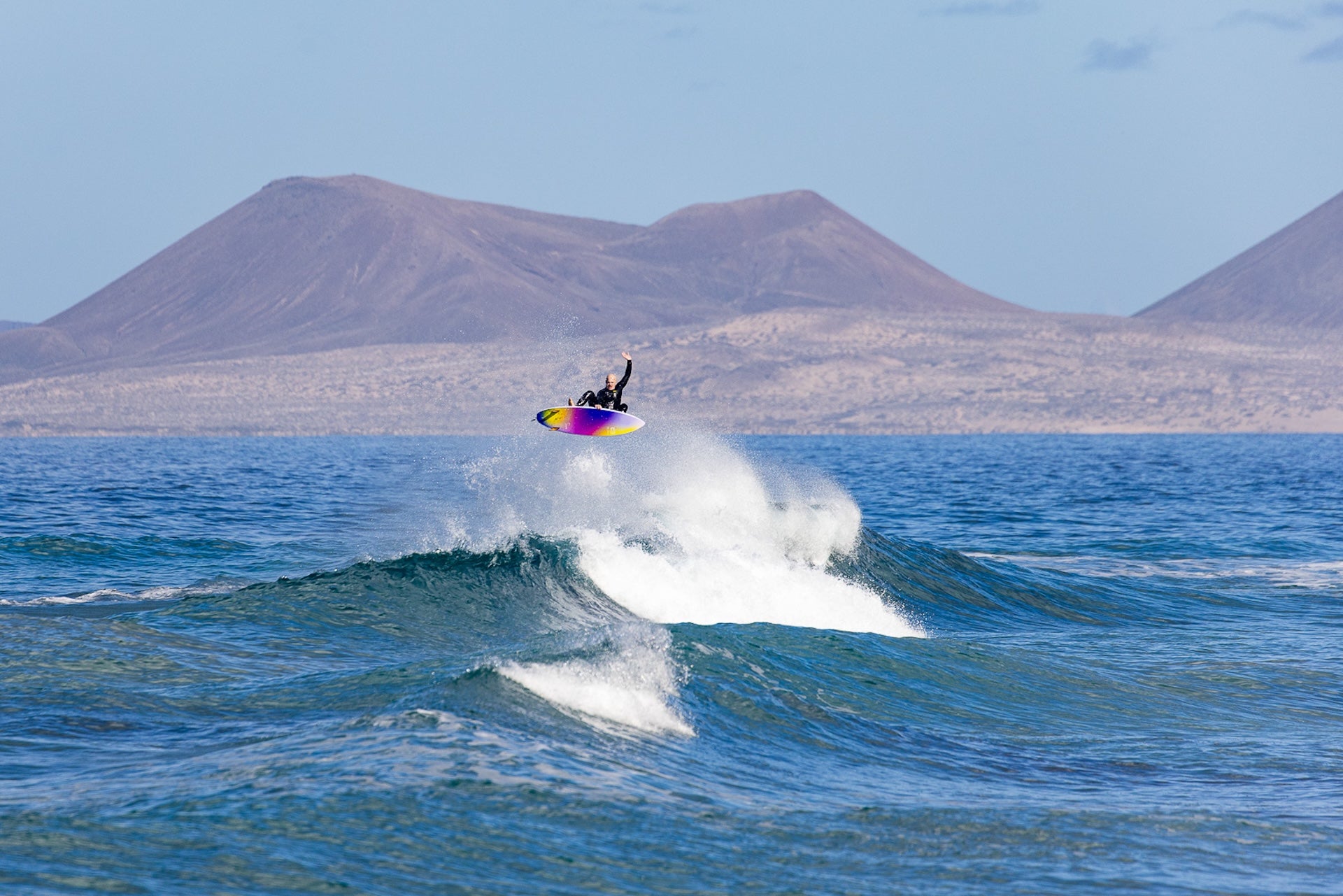 un surfeur en train de faire un arial avec une planche de surf Zeus x Cabianca, il essaye de faire un signe comme Medina