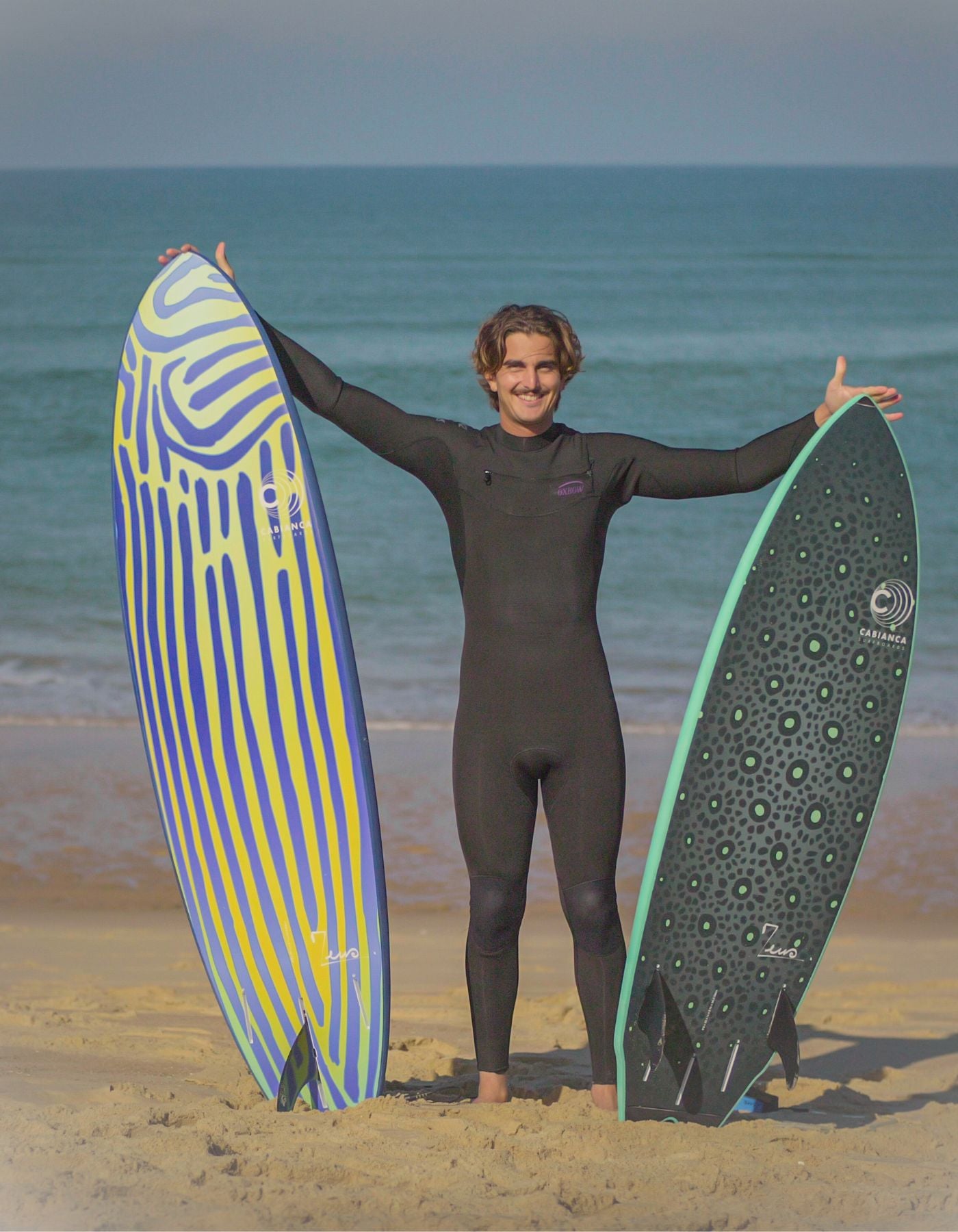 Un surfeur sur la plage de lacanau combinaison de surf noir oxbow et deux planche de surf de type shortboard