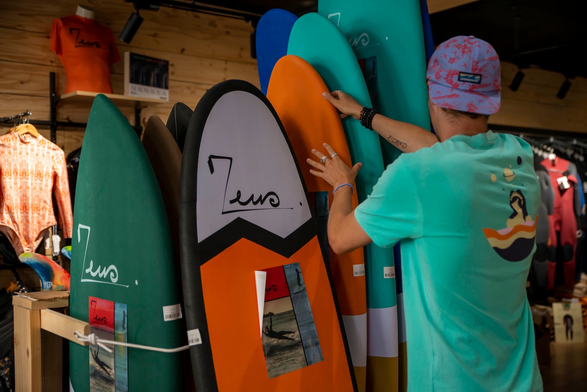 un vendeur en train de sortir une planche de surf orange d'un rack dans un magasin de surf