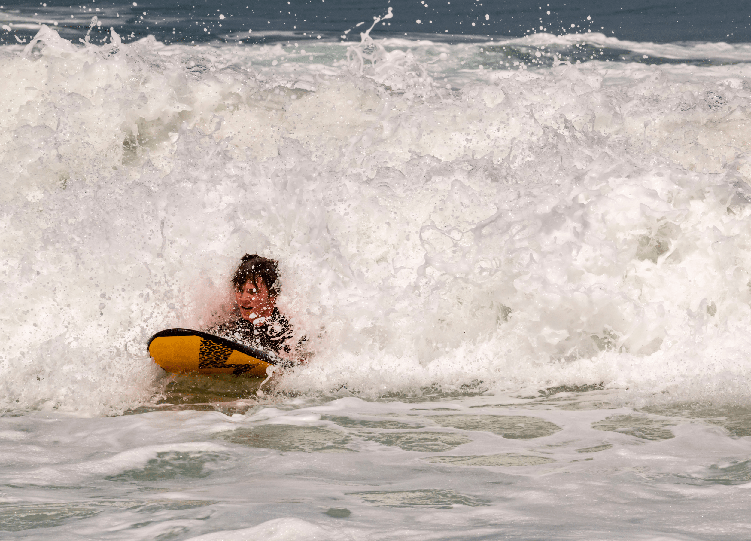 Surfer en position allongé sur une planche de surf en mousse en train de surfer la mousse d'un vague 