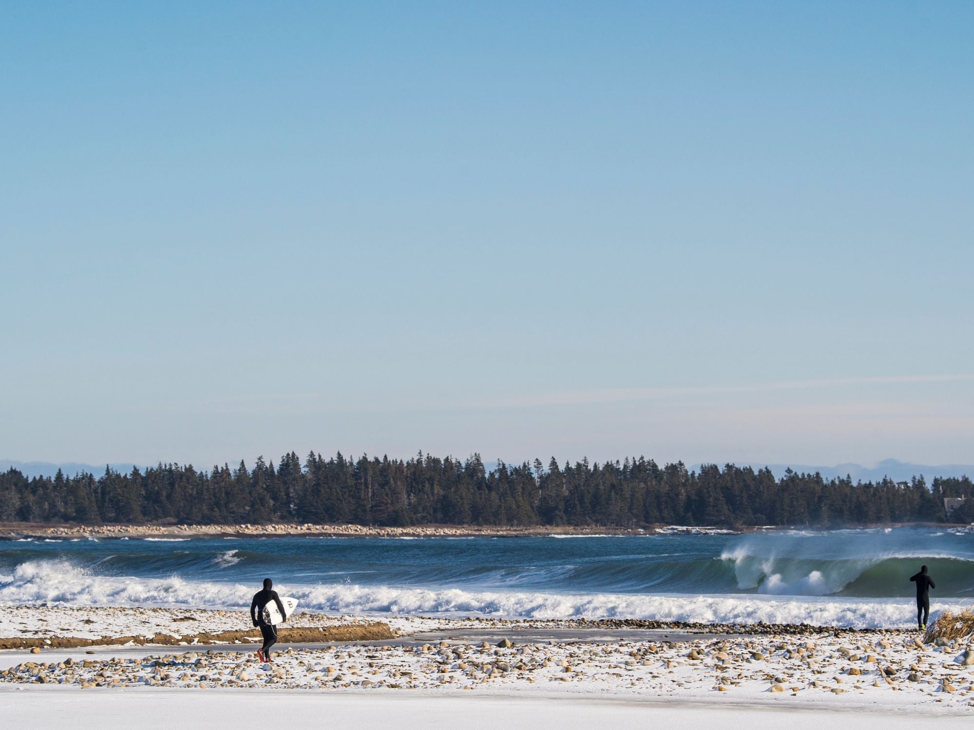 un surfeur en train de marcher sur une plage enneigée