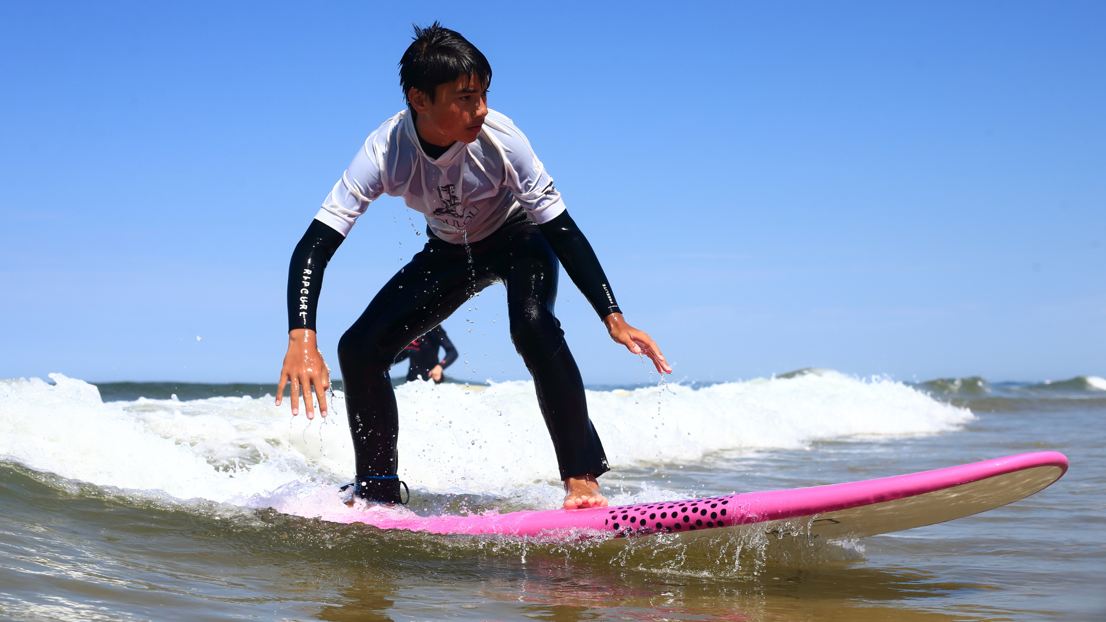 Surfeur débutant à l'eau sur une planche Zeus avec son équipement combinaison et lycra