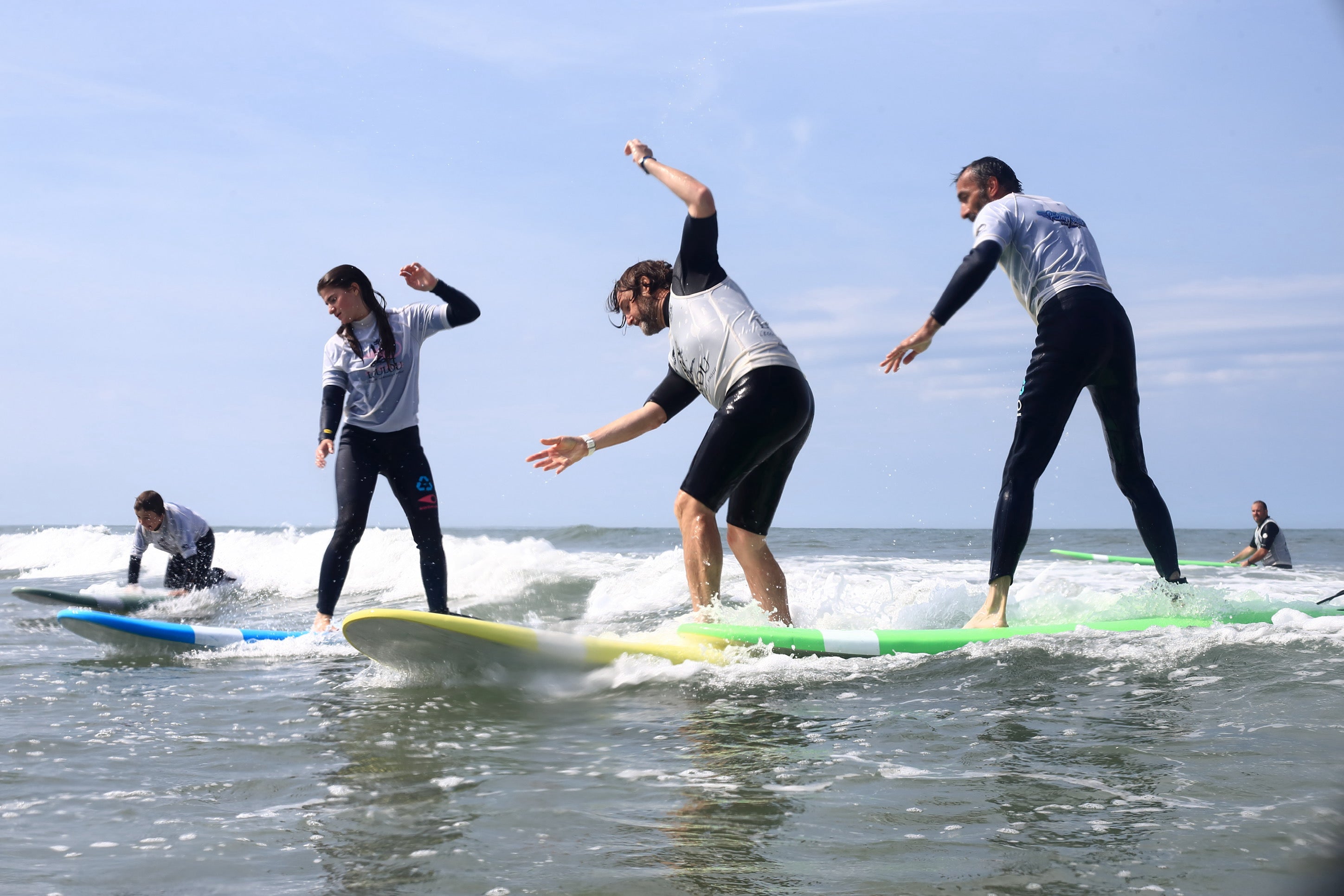 Surfers débutants pendant un cour de surf en france en train de prendre une vague pendant un cours de Surf en France sur des planches de surf en mousse des marques zeus et softech.