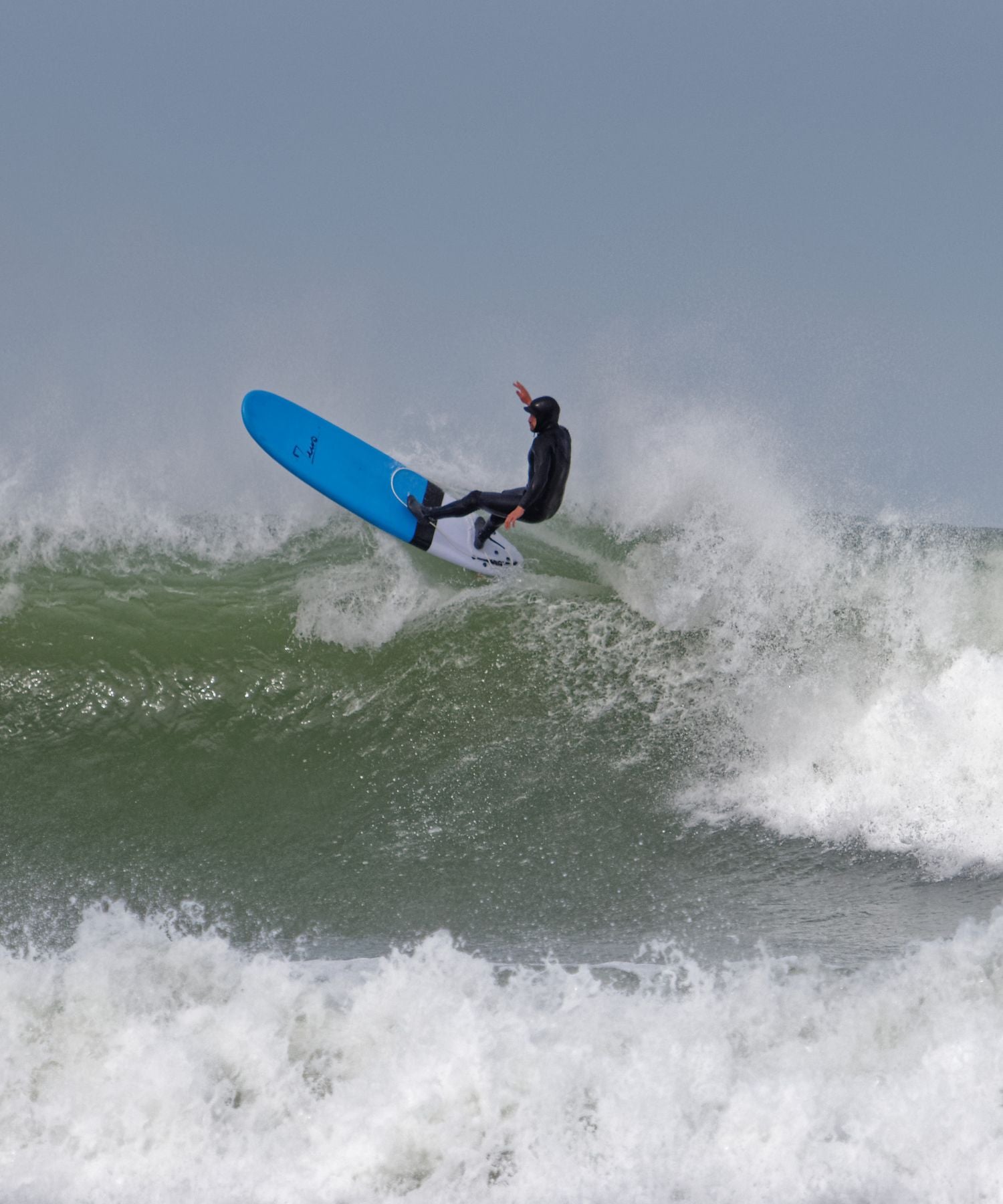 Surfeur sur une grosse vague avec une planche de surf en mousse bleu de la marque Zeus 
