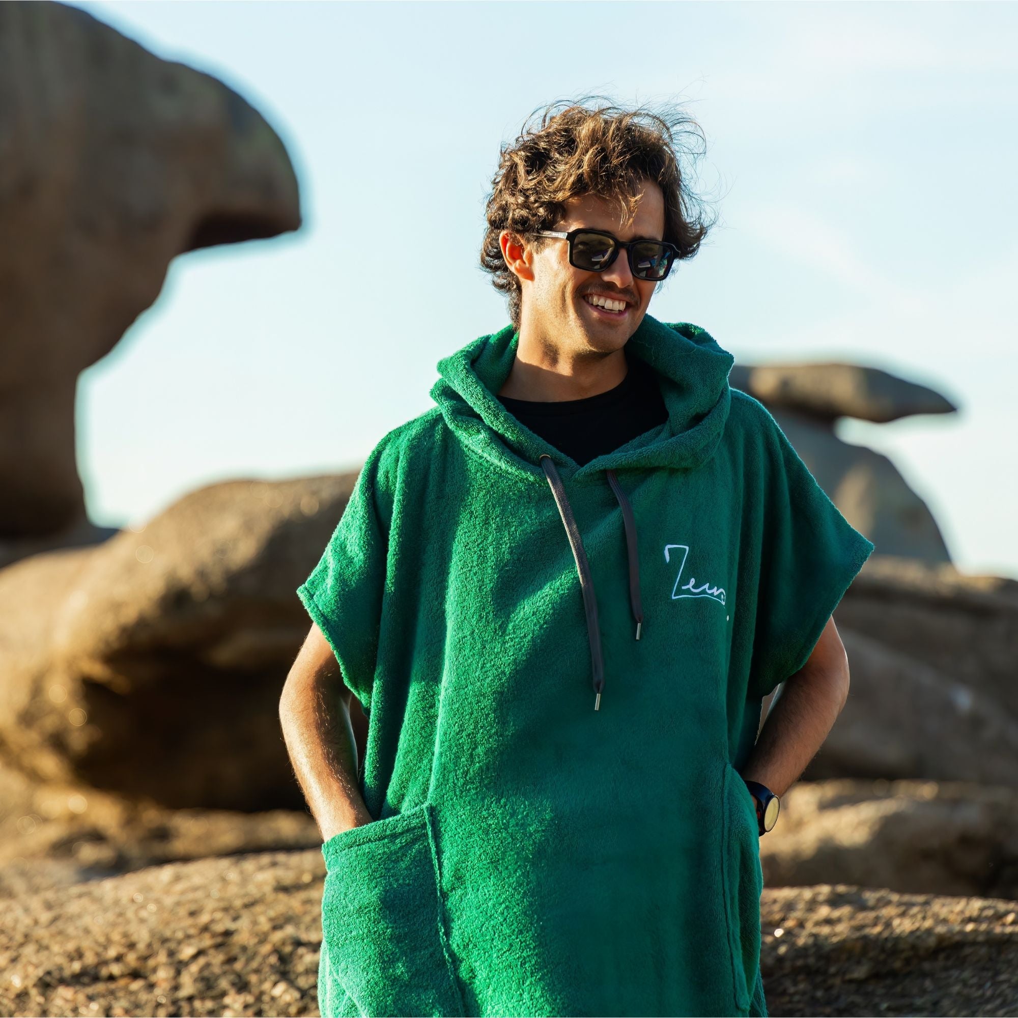 a man wearing a green hooded sweatshirt standing in front of a rock formation