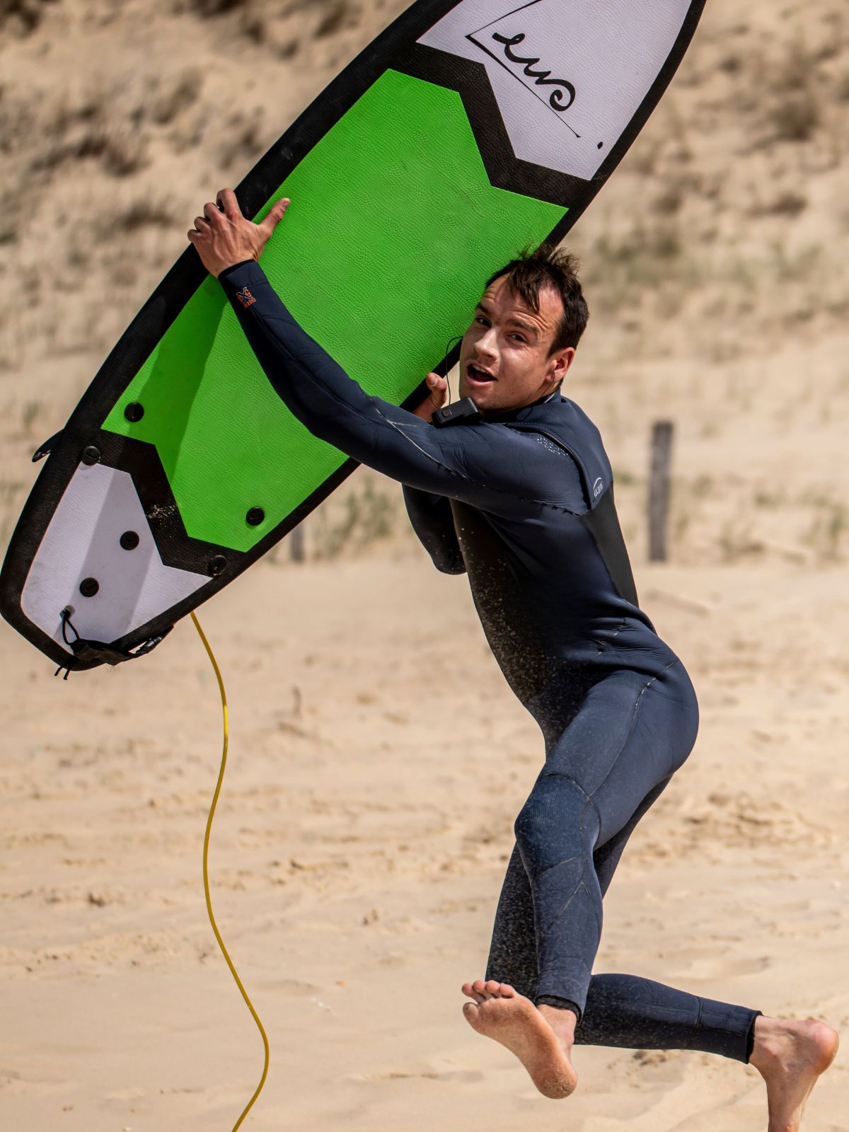 un surfeur en combinaison de surf oxbow avec une planche de surf en mousse verte zeus dans les bras sur la plage 