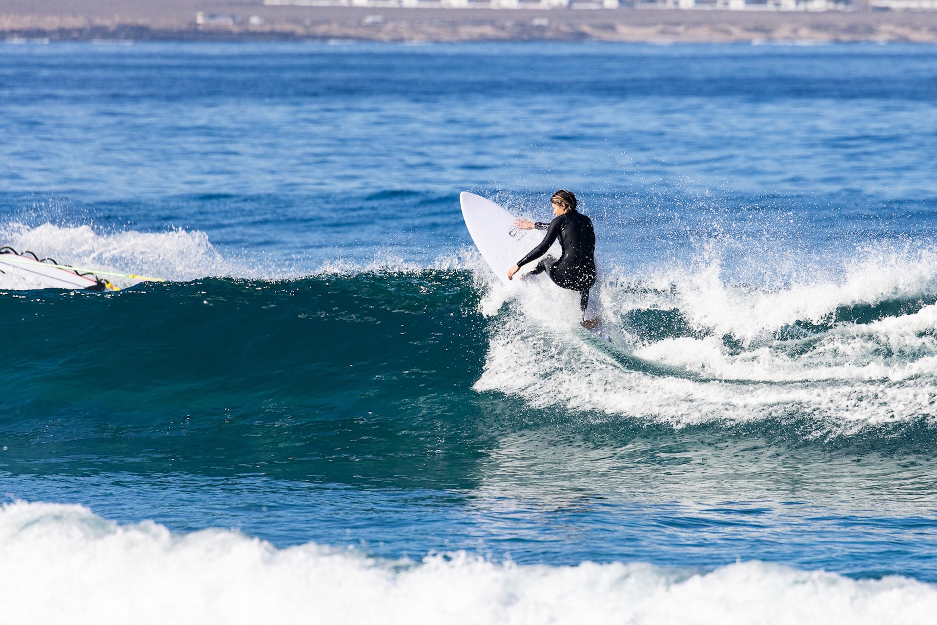 Une surfeuse de niveau intermédiaire en train de faire un virage agressif sur la crête de la vague avec une planche de surf zeus de couleur blanche 