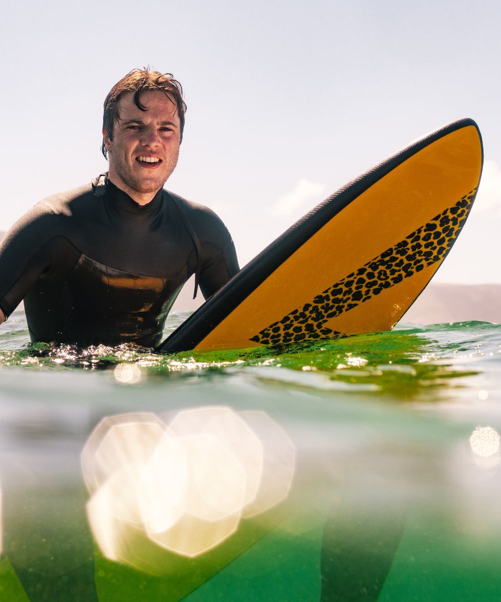 un surfeur en train d'attendre au pic sur une planche de surf en mousse jaune de la marque Zeus